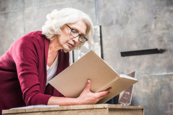 woman reading book with laptop - deposit photos